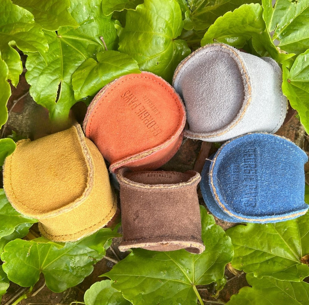 A colorful collection of small suede jewelry pouches scattered artistically among vibrant green leaves and a Georgie Paws Ball - Gold.