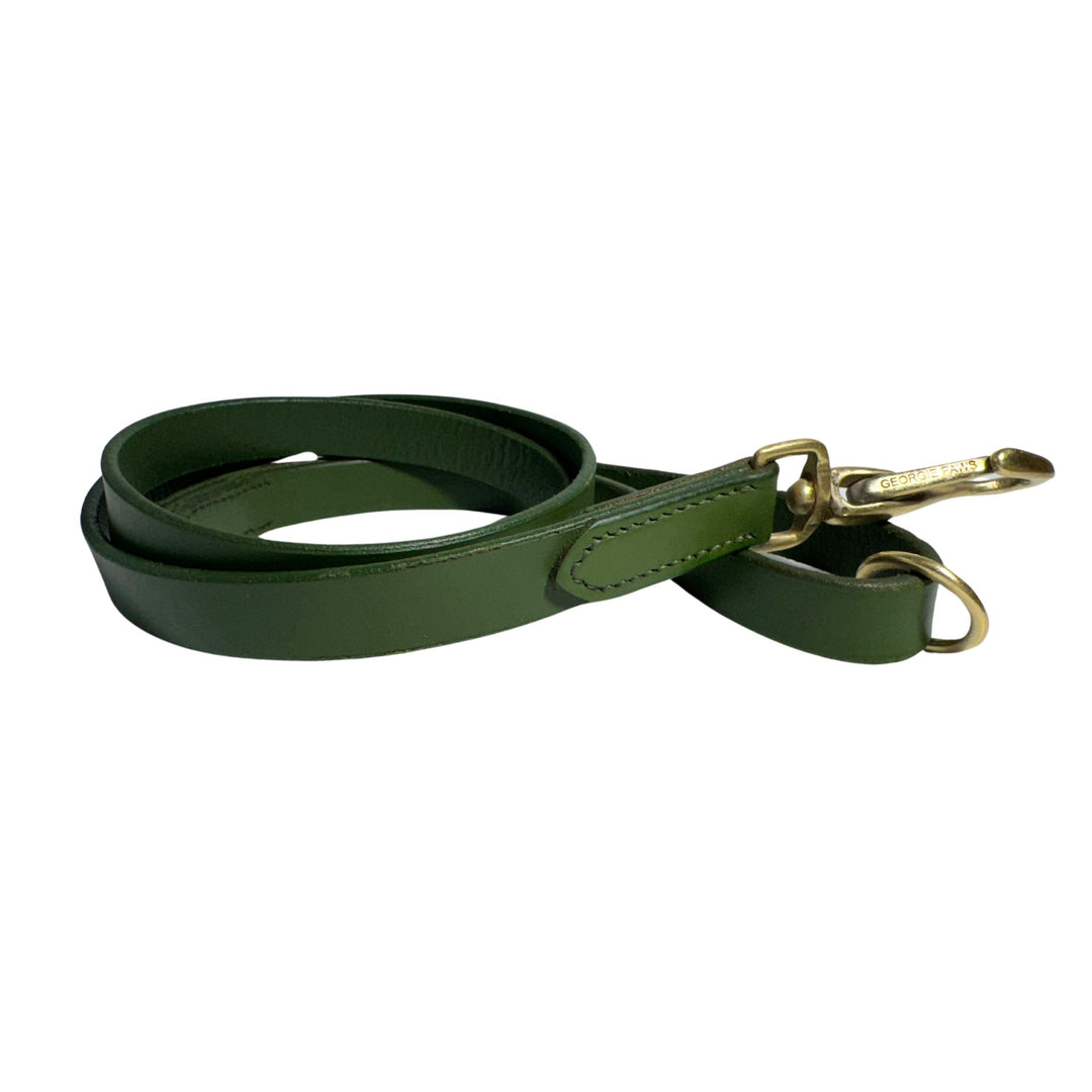 A coiled green buffalo leather dog leash with an antique brass clasp and D-ring. The leash features visible stitching along the edges, creating a sleek and durable appearance. With a Lyndal Loop handle, it combines functionality with an elegant design, perfect for attaching to a dog collar. Introducing the Bald Lead Chive by Georgie Paws.