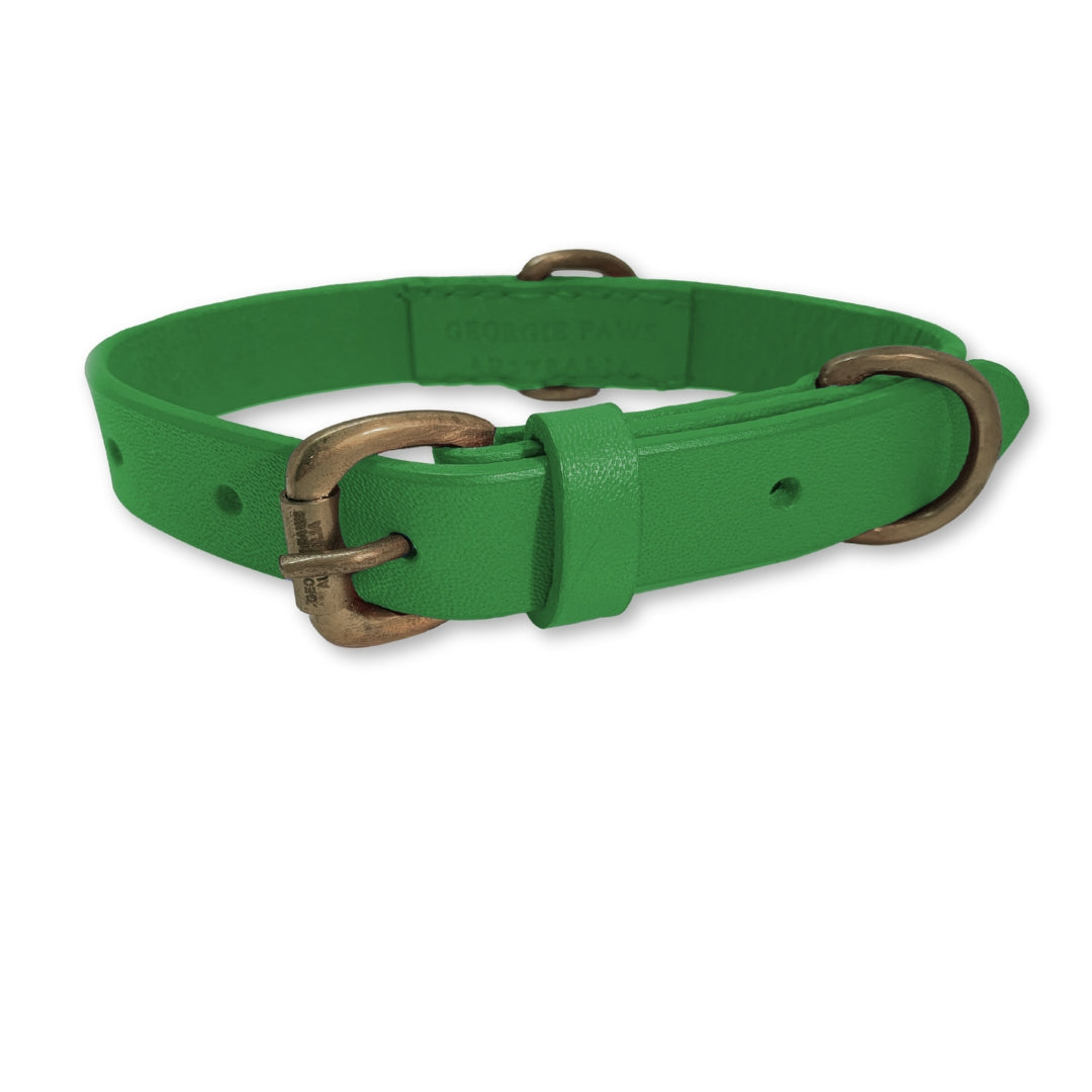 The "Bald Collar - Green" by Georgie Paws is a bright green handmade buffalo leather dog collar with antique brass hardware. It features small punched holes for adjustability, a loop near the buckle to secure excess strap, and the brand name subtly embossed on the smooth-textured inner side.