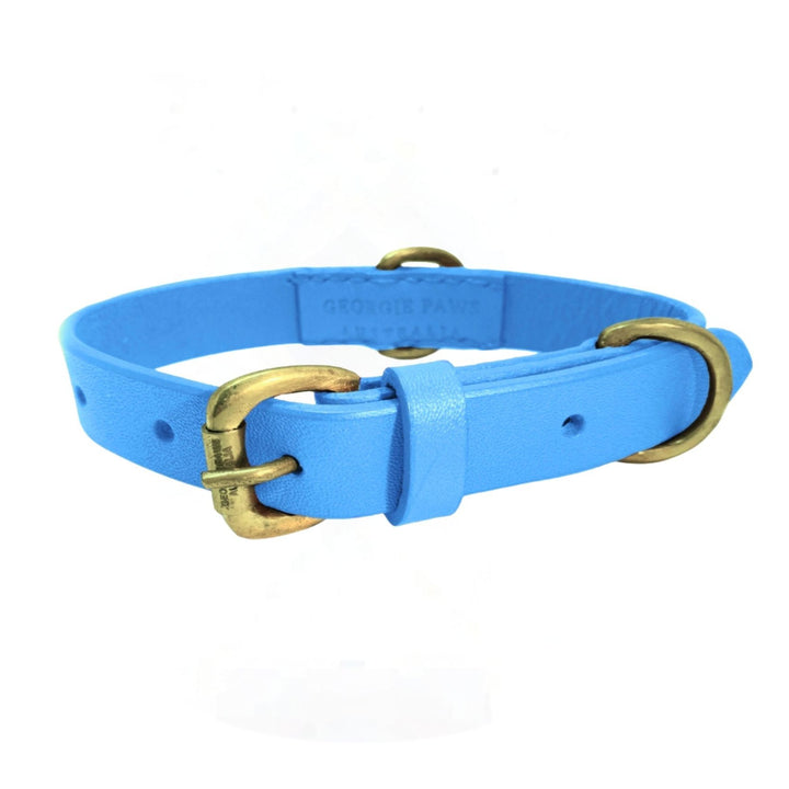 The Blue Dog Collar by Georgie Paws is handmade from buffalo leather in light blue, with antique brass buckle, loop, and D-ring. It features adjustment holes and embossed branding inside. Shown on a plain white background.