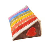 The Georgie Paws Rainbow Cake Toy is a vibrant, wedge-shaped pillow with pink, blue, green, yellow, orange, and white stripes. It features a red heart embroidered on brown fabric at the narrow end and visible stitching for a handmade look.