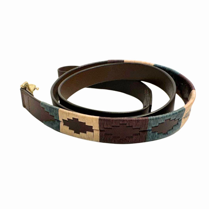 The Georgie Paws Polo Collar - Dean, crafted from brown buffalo leather with beige, blue, and dark brown geometric patterns, is coiled to reveal a small brass buckle. Its hand-stitched design echoes artisanal craftsmanship against a plain white background.