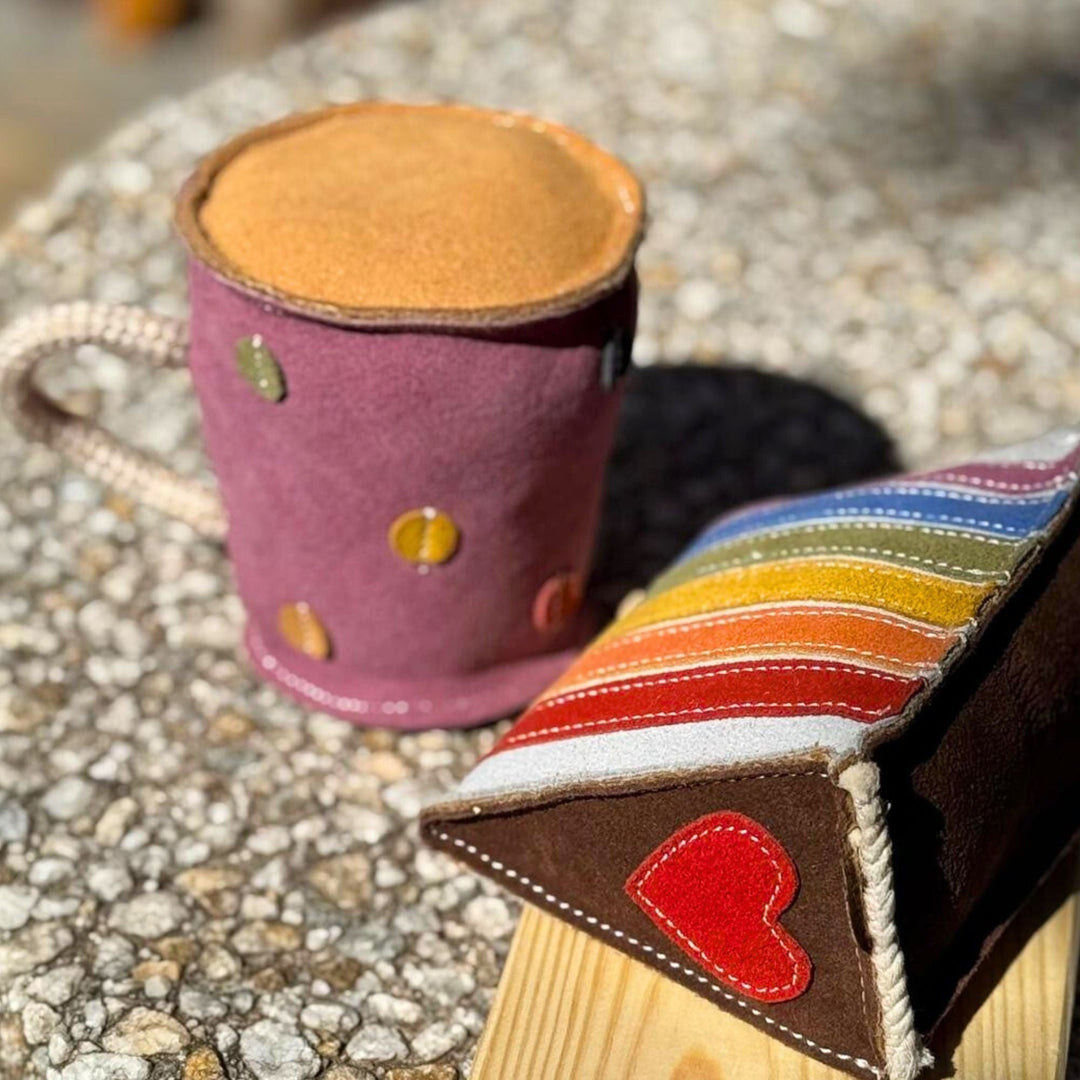 A styled photo of the Rainbow Cake Dog Toy by Georgie Paws next to a cup of tea, showing the colorful layered fabric cake-shaped dog toy.