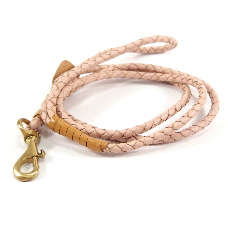 The Windsor Lead - Carnation by Georgie Paws is a coiled, light pink braided leather dog leash made from durable buffalo leather. It includes a brass hook clasp for effortless attachment to the collar and is adorned with chic decorative tan accents near the clasp.