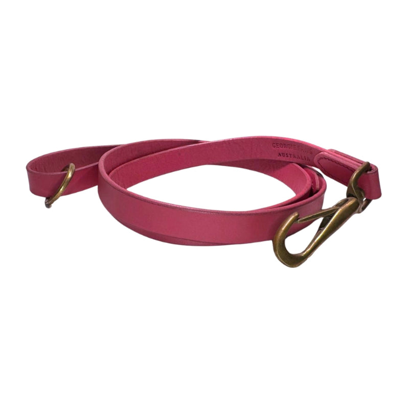 The Bald Lead Hot Pink by Georgie Paws is a coiled, pink dog leash made from vegetable tanned buffalo leather with gold metal hardware, including a clasp and a D-ring. Visible stitching along the edges reinforces the leather, and the leash is displayed on a white background.