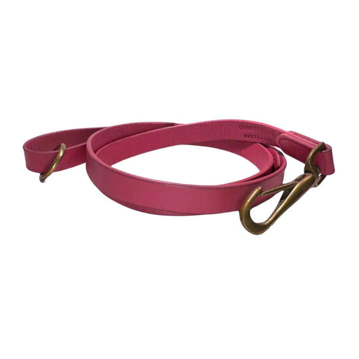 The Bald Lead Hot Pink by Georgie Paws is a coiled, pink dog leash made from vegetable tanned buffalo leather with gold metal hardware, including a clasp and a D-ring. Visible stitching along the edges reinforces the leather, and the leash is displayed on a white background.