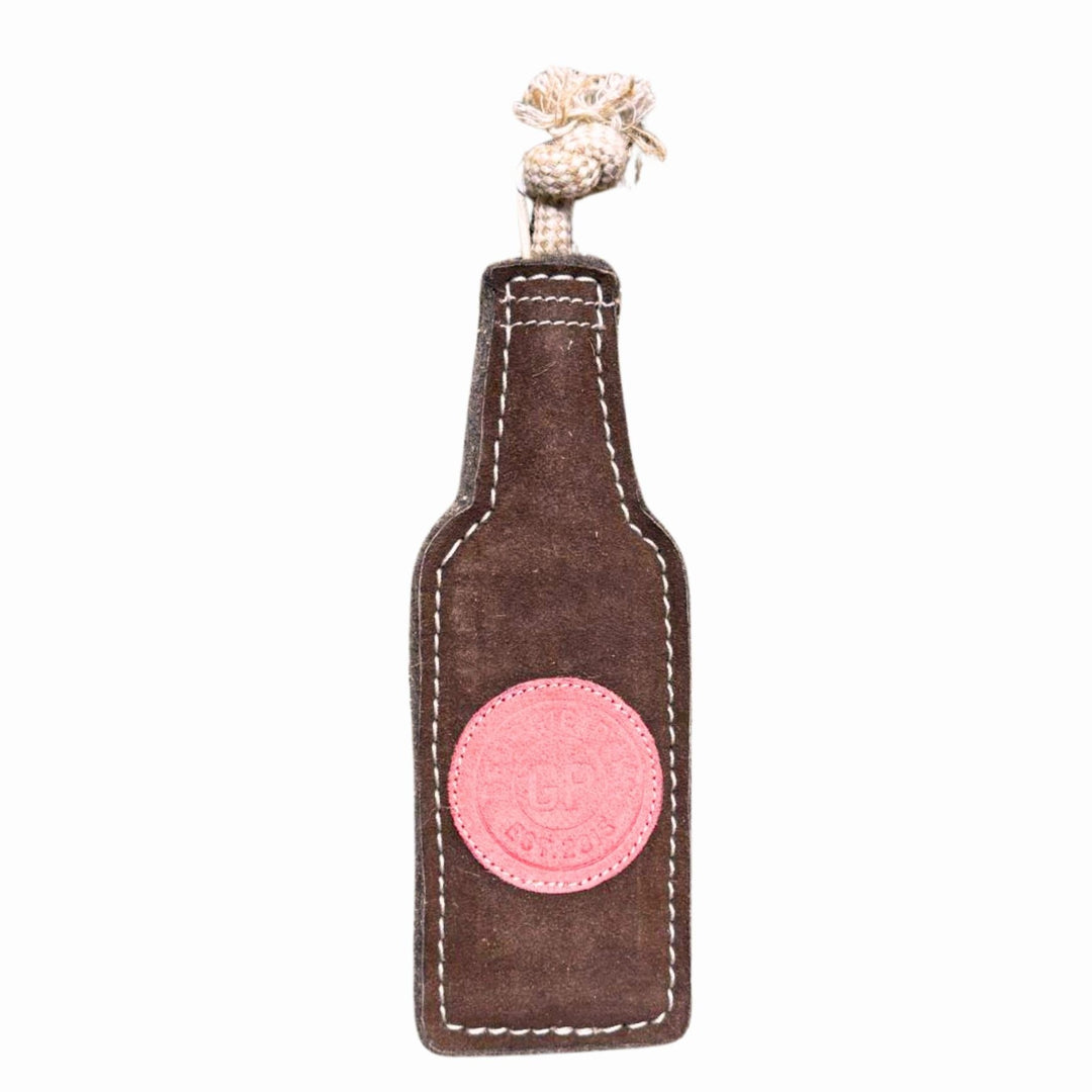 The Georgie Paws Bevvy Dog Toy is a durable, beer bottle-shaped toy made of brown fabric with white stitching, a pink patch, and a knotted beige rope handle. Shown on a white background.