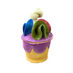 Meet the Pixie Cake toy by Georgie Paws—a whimsical plush cupcake perfect for small dogs. It features a yellow base, purple top with vibrant felt toppings in wavy blue, green, red shapes, and a soft beige stem resembling a playful candle.