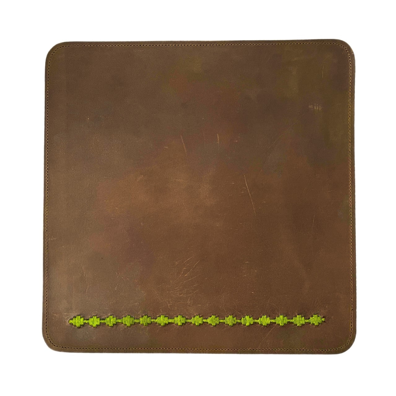 A worn brown buffalo leather dinner mat with visible scratches and distress marks. The mat has rounded corners and is stitched with a contrasting light thread. A decorative row of small, embossed green shamrocks from Georgie Paws.