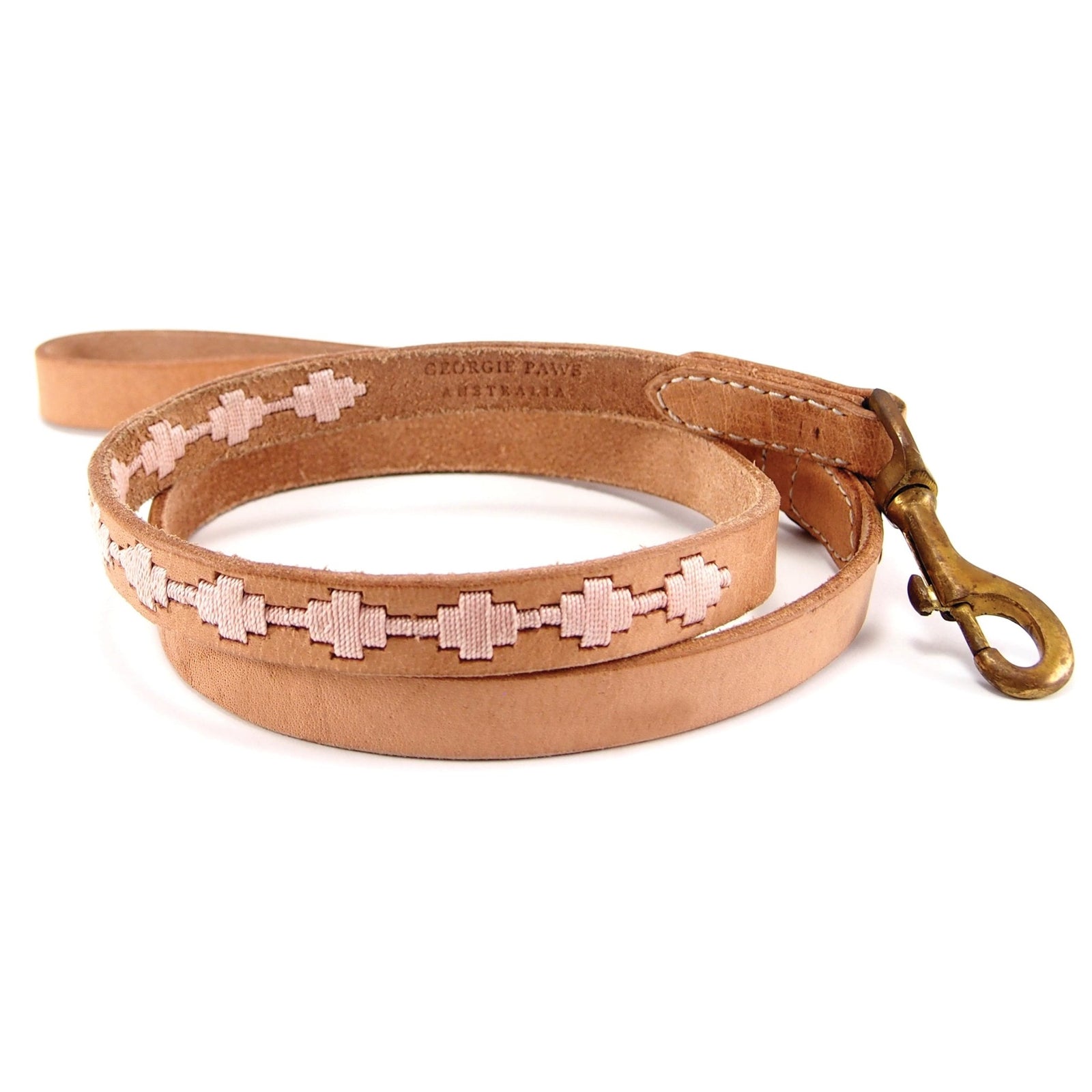 The Ethel Lead - Carnation by Georgie Paws is a tan, vegetable-tanned buffalo leather dog leash with a brass clasp, adorned along its length with pink geometric embroidery. Handmade and designed with a looped handle, the smooth, slightly shiny leather features the Georgie Paws logo embossed near the handle.