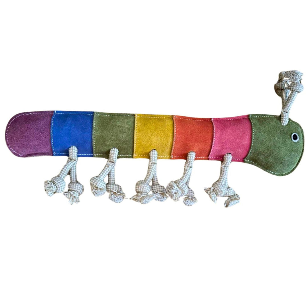 The Giant Rainbow Gerti by Georgie Paws is a colorful plush caterpillar toy featuring sections in purple, blue, green, yellow, orange, and pink. Made with compost-friendly materials, it has a smiling green head with eyes and knotted rope legs. Segments are stitched around biodegradable coconut fiber.