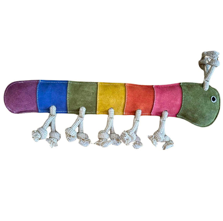 The Giant Rainbow Gerti by Georgie Paws is a colorful plush caterpillar toy featuring sections in purple, blue, green, yellow, orange, and pink. Made with compost-friendly materials, it has a smiling green head with eyes and knotted rope legs. Segments are stitched around biodegradable coconut fiber.