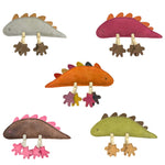 Five eco-friendly plush Larry Lizard toys from Georgie Paws, each in different colors (gray, maroon, orange, brown, and green), are arranged in a semicircle. These toys feature X-shaped eyes, small spikes along the back, and dangling rope legs with felt feet that match their body colors.