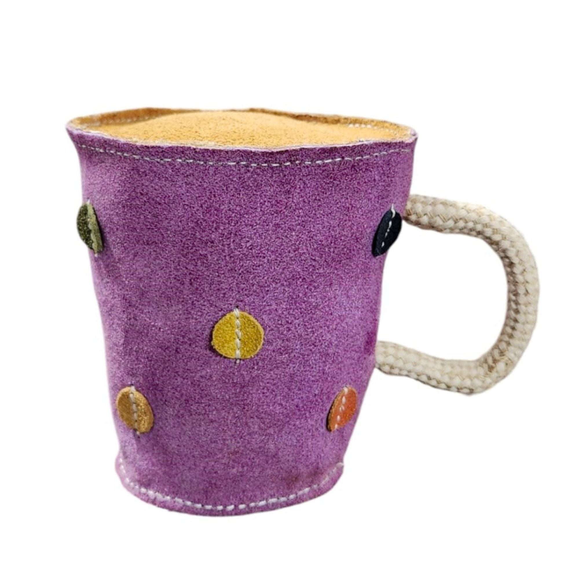 The Georgie Paws "Tea in a Mug Toy" features a plush purple fabric with multicolored circular patches, a white crocheted-texture handle, and is filled with tea. Its surface has the soft appearance of buffalo suede.