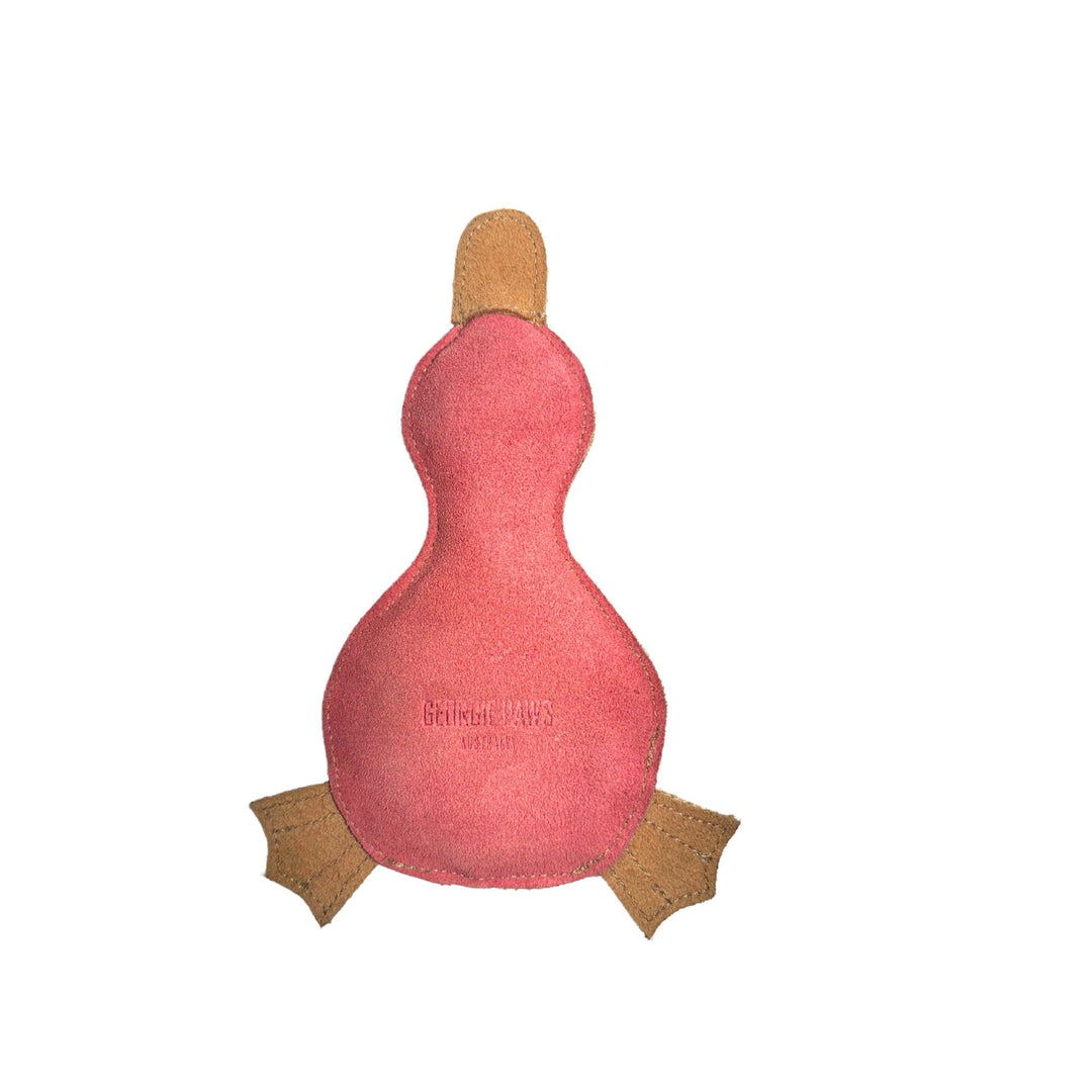 A simple pink platypus-shaped dog toy called "Paul the Playtpus - Chive" from Georgie Paws, made from natural, vegetable-tanned buffalo leather suede, features brown webbed feet and a brown beak. The words "GENUINE LEATHER" are printed in small letters on the surface. The toy has no facial features and is photographed against a plain white background.