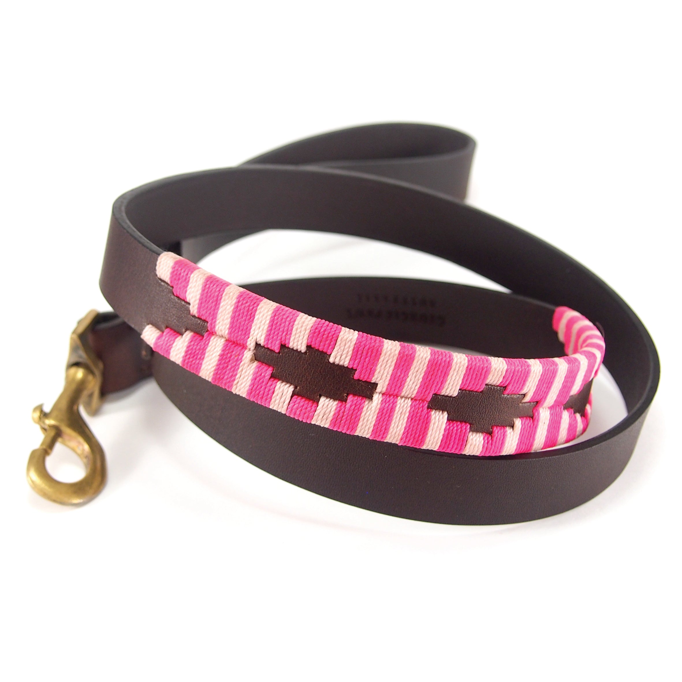 Introducing the Polo Lead - Pinky by Georgie Paws, a handmade dog leash adorned with a brown Buffalo Leather strap and a vibrant pink and brown woven pattern. This stylish leash features a brass metal clasp for secure attachment. Displayed in a loose coil on a white background, it showcases its colorful design and robust construction beautifully.