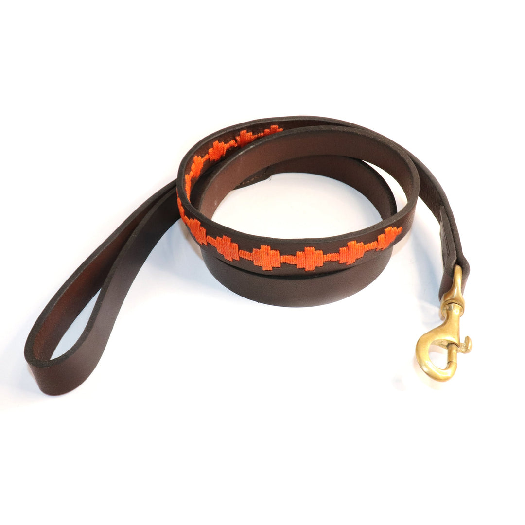 Introducing the Polo Bark Lead - Ochre by Georgie Paws: a handmade, plastic-free dark brown leather dog leash featuring a sturdy brass clasp and an orange ochre embroidered pattern near the handle. The coiled leash is displayed on a white background, showcasing its decorative stitching and durable construction.