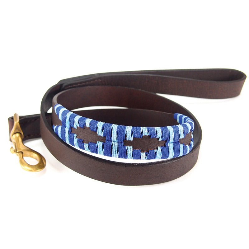 The Polo Lead - Bluey by Georgie Paws is coiled on a white background. This dog leash is crafted from brown vegetable tanned buffalo leather and features a looped handle wrapped with blue and white cord. A brass clasp provides secure attachment to a collar. Sturdy, well-crafted, and handmade for durability and comfort, this leash offers a sustainable choice for pet owners.