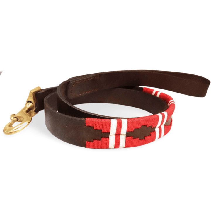 A neatly coiled Polo Lead - Kaliman dog leash by Georgie Paws is displayed on a white background. Crafted from natural dark brown leather and finished with a brass clasp, part of the leash features red and white geometric stitched patterns that lend it a handmade appearance.