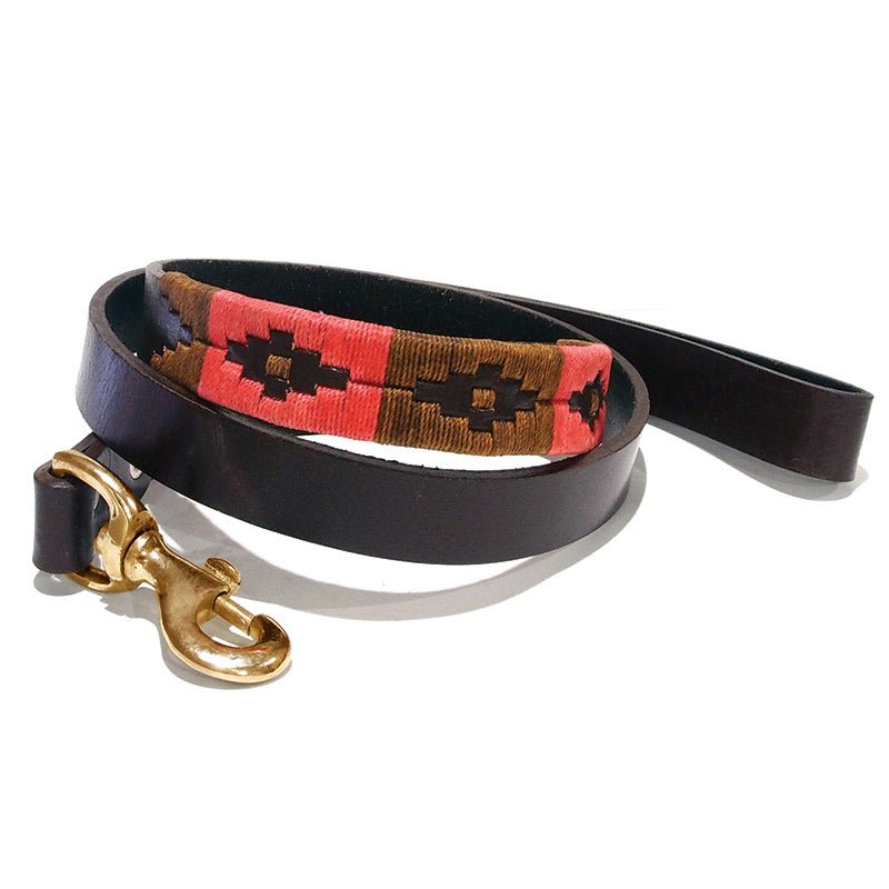 The Georgie Paws Polo Lead - Poppy is a brown vegetable tanned buffalo leather dog leash with a gold metal clasp, featuring a red and brown woven pattern accented by black geometric designs along part of the strap, coiled neatly against a white background.