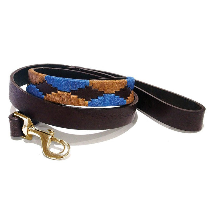 The Polo Lead - Stubble by Georgie Paws is a handmade brown leather dog leash with a gold metal clasp, showcasing a stitched pattern of blue, tan, and dark brown geometric shapes on part of the lead. Crafted from natural materials, the leash is neatly coiled against a white background.