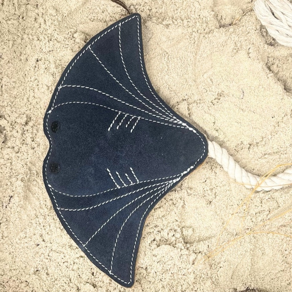 A handmade Simon the Stingray - navy toy with white stitching details lies on a sandy surface, accompanied by a braided white rope for pretend play. (Brand Name: Georgie Paws)