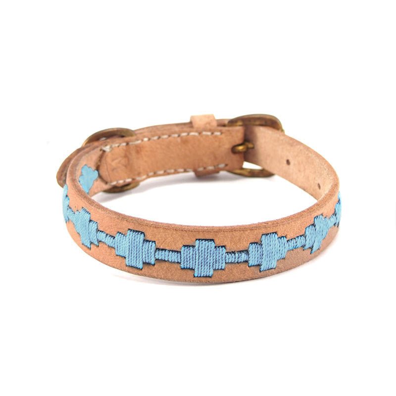 The Ethel Collar - Chambray by Georgie Paws features vegetable-tanned buffalo leather in a tan hue, adorned with a chain-like pattern of light blue geometric shapes stitched along its center. Finished with a gold buckle, this collar’s smooth and unfinished interior highlights its natural, plastic-free craftsmanship.