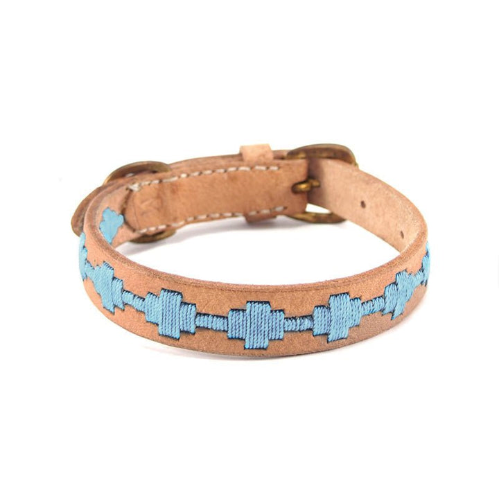 The Ethel Collar - Chambray by Georgie Paws features vegetable-tanned buffalo leather in a tan hue, adorned with a chain-like pattern of light blue geometric shapes stitched along its center. Finished with a gold buckle, this collar’s smooth and unfinished interior highlights its natural, plastic-free craftsmanship.