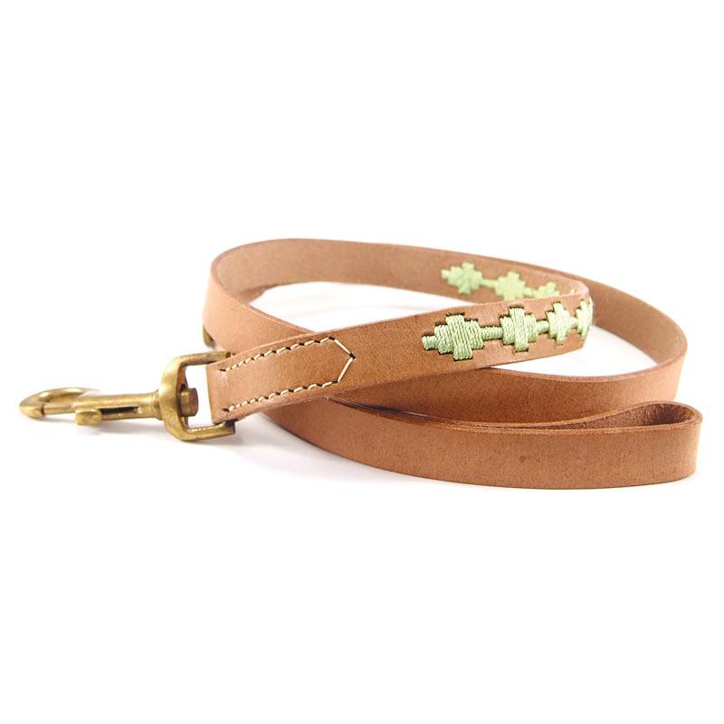 The Ethel Lead - Pear Green by Georgie Paws is a tan leather dog leash, handmade and decorated with cross-like green embroidered stitches near the handle. It features a brass clasp, visible stitching near the hardware, and is crafted to be smooth, sustainable, and plastic-free. The leash is shown loosely coiled on a white surface.