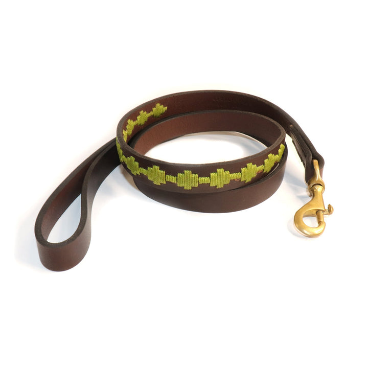 The Polo Bark Lead - Grass by Georgie Paws is a handmade brown vegetable-tanned buffalo leather dog leash, coiled neatly on a white background. It features a loop handle, a yellow-green stitched geometric pattern along its length, and is finished with a brass swivel snap hook for durability and style.